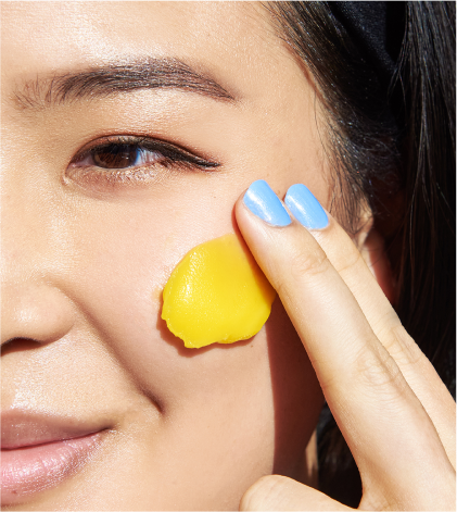 Close-up of a woman applying yellow cream to her face with a finger.
