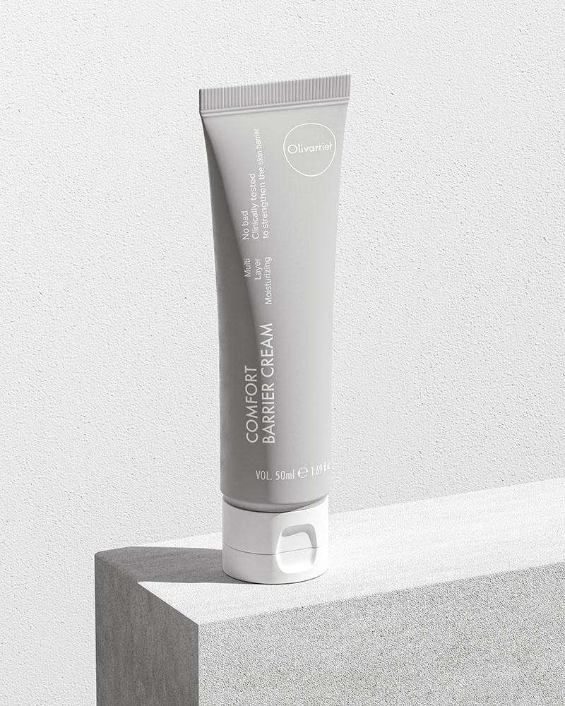 Olivarrier comfort barrier relief cream lifestyle image - the white bottle resting on a white block with wooden texture, against a white background